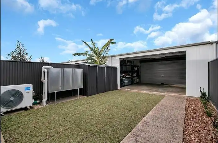 Rear lawn with a paved path, rainwater tank, air-conditioning unit and a garage with its roller door open