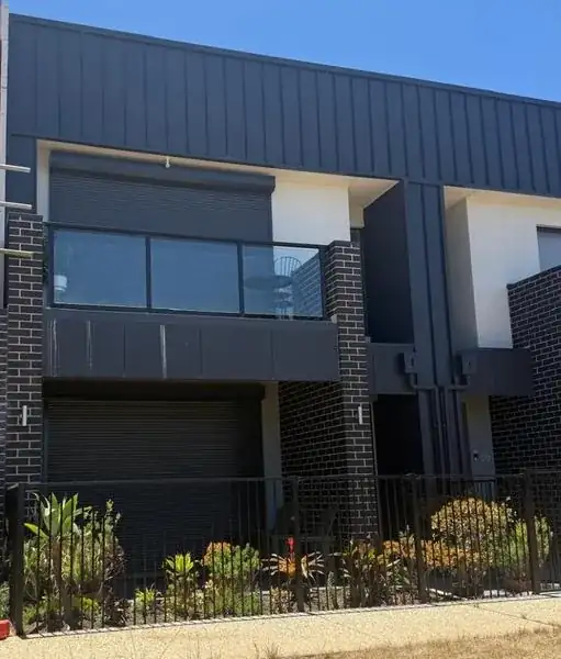 Two-storey home with dark cladding, a brick base, an upper balcony and landscaped front garden