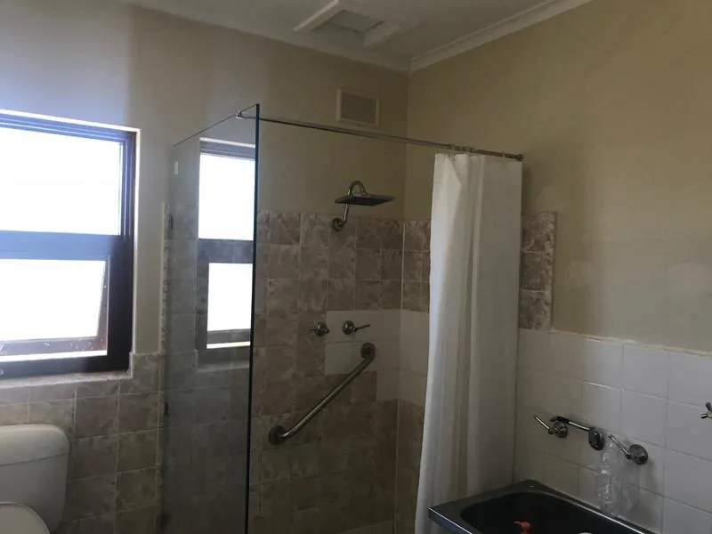 Bathroom shower with glass screen and grab rail, beside a bath and laundry trough
