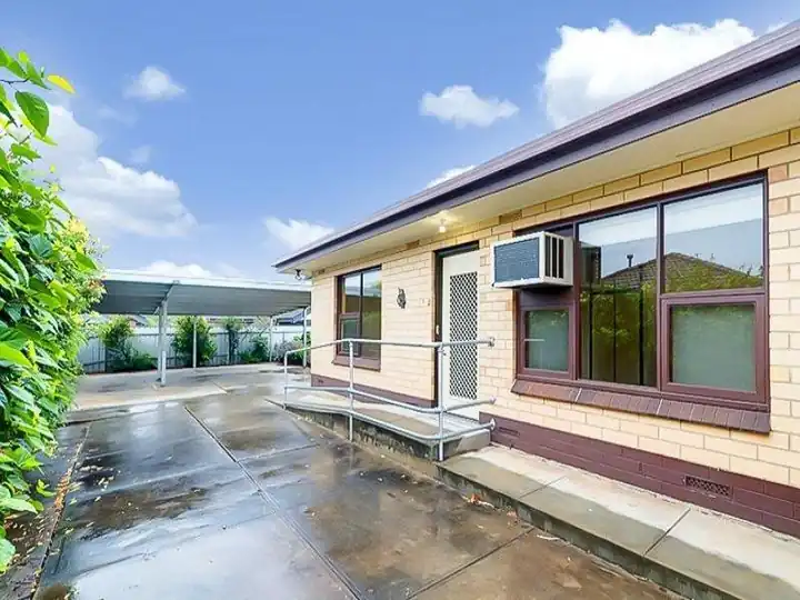 Front entrance with handrails at the door, a wall air conditioner and the carport behind
