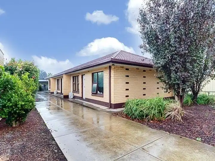 Cream-brick unit with a tiled roof, garden beds, an established tree and a paved path leading to the entrance
