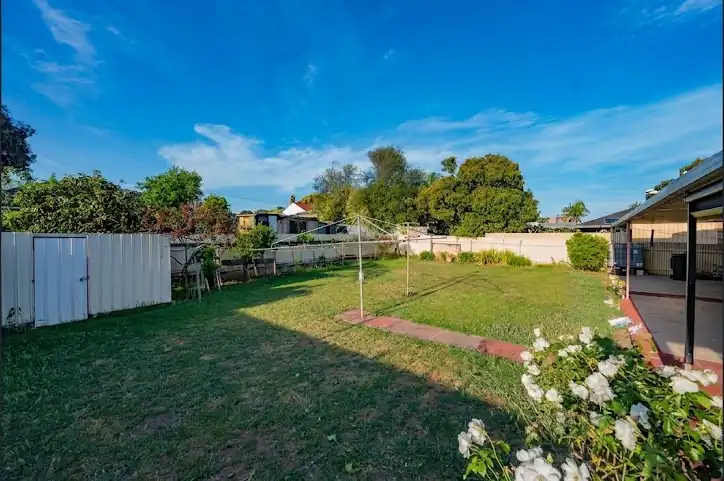 Large fenced back lawn with rotary clothesline, established rose bushes and a covered verandah along the rear of the house
