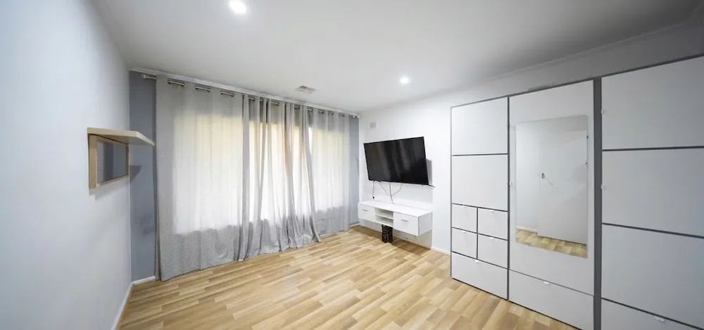 Bedroom with mirrored built-in robes, a wall-mounted television and timber-look flooring