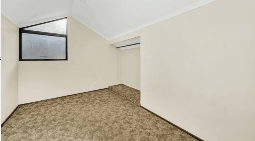 Bedroom with a raked ceiling, patterned carpet and a high obscure-glass window