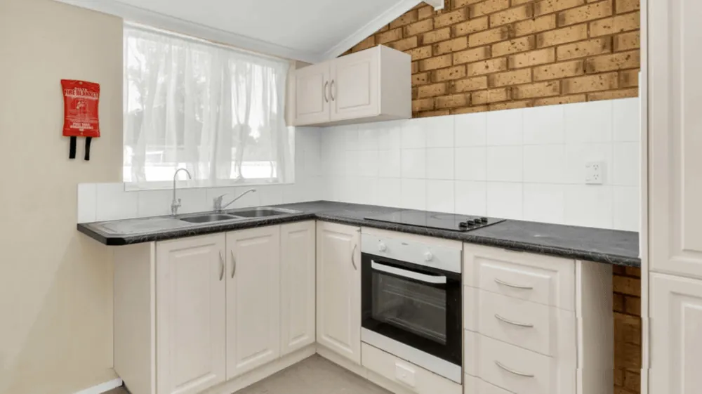 Kitchen with electric cooktop, under-bench oven, double sink and a wall-mounted fire blanket