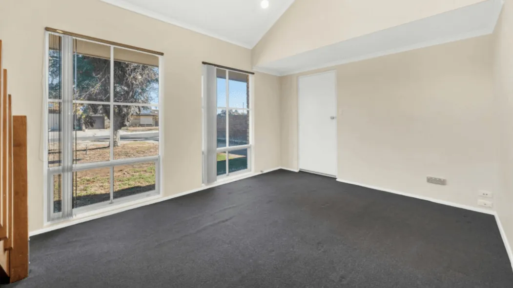 Open-plan living area with a vaulted ceiling, charcoal carpet and large front windows